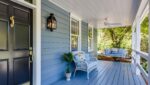 A porch with blue siding and white furniture.