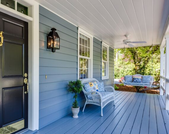 A porch with blue siding and white furniture.