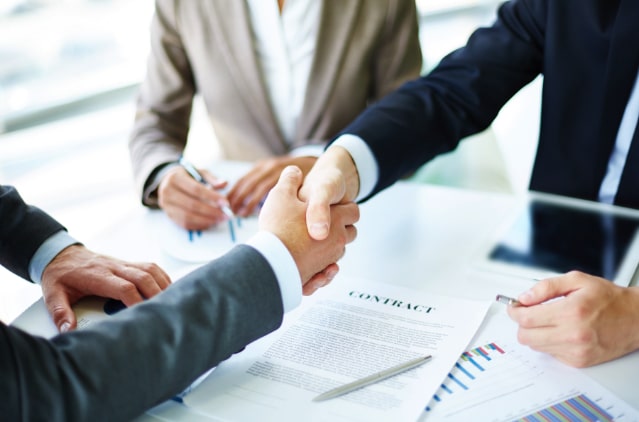 A group of people shaking hands over paperwork.