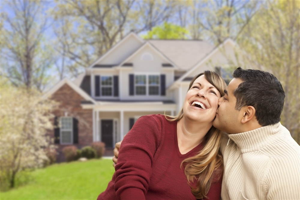 A man and woman are kissing in front of their house.